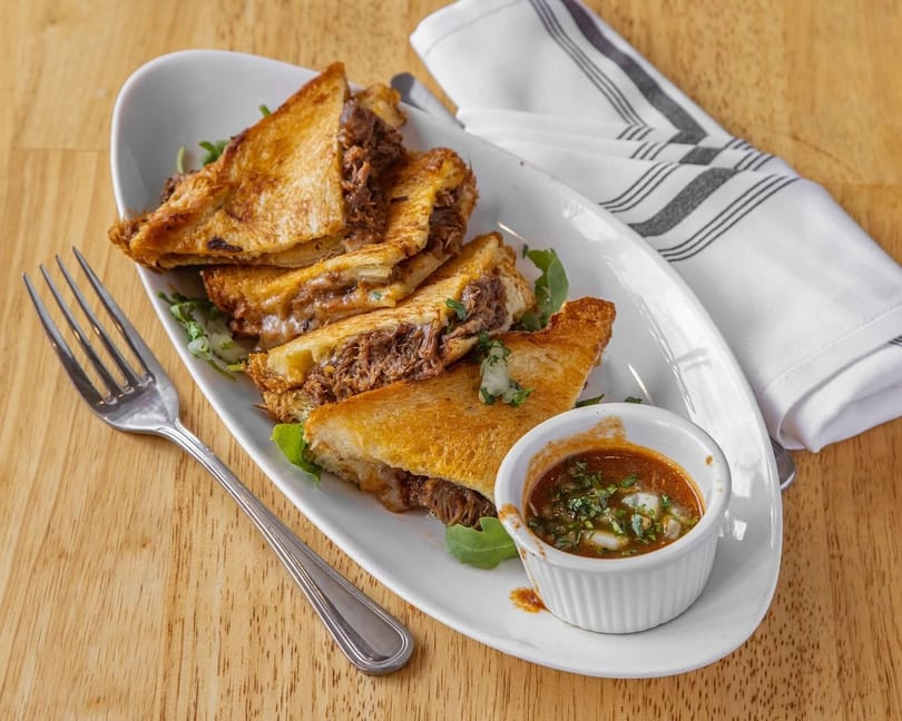 Golden grilled cheese sandwiches filled with shredded meat, served with a dipping sauce and fork.