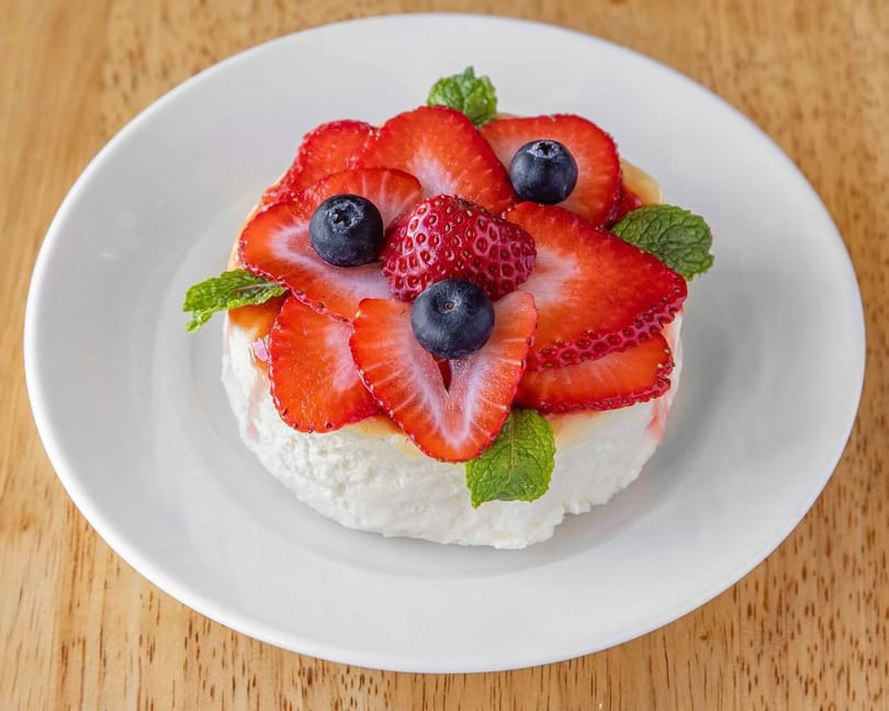A white dessert topped with sliced strawberries, whole blueberries, and mint leaves on a white plate.