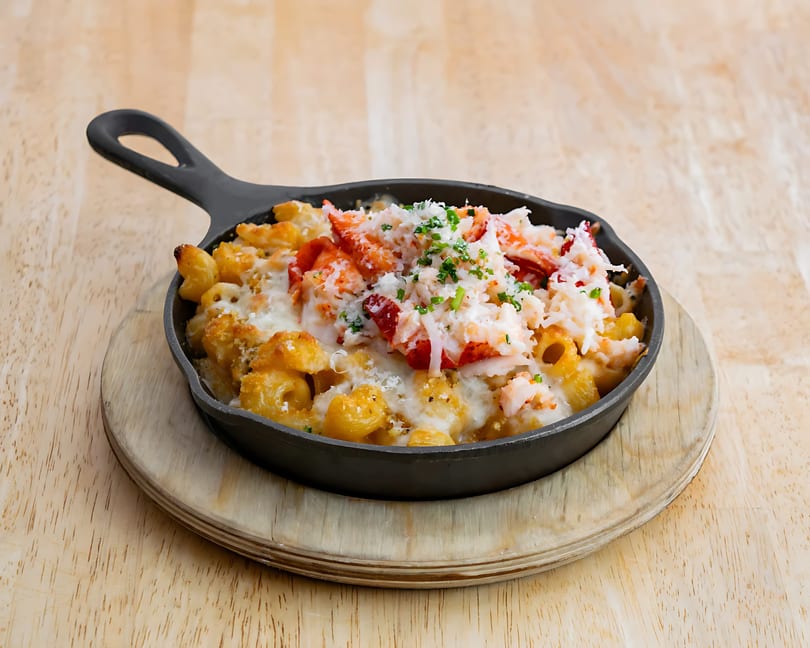 Lobster mac and cheese in a black cast iron skillet on a wooden serving board.
